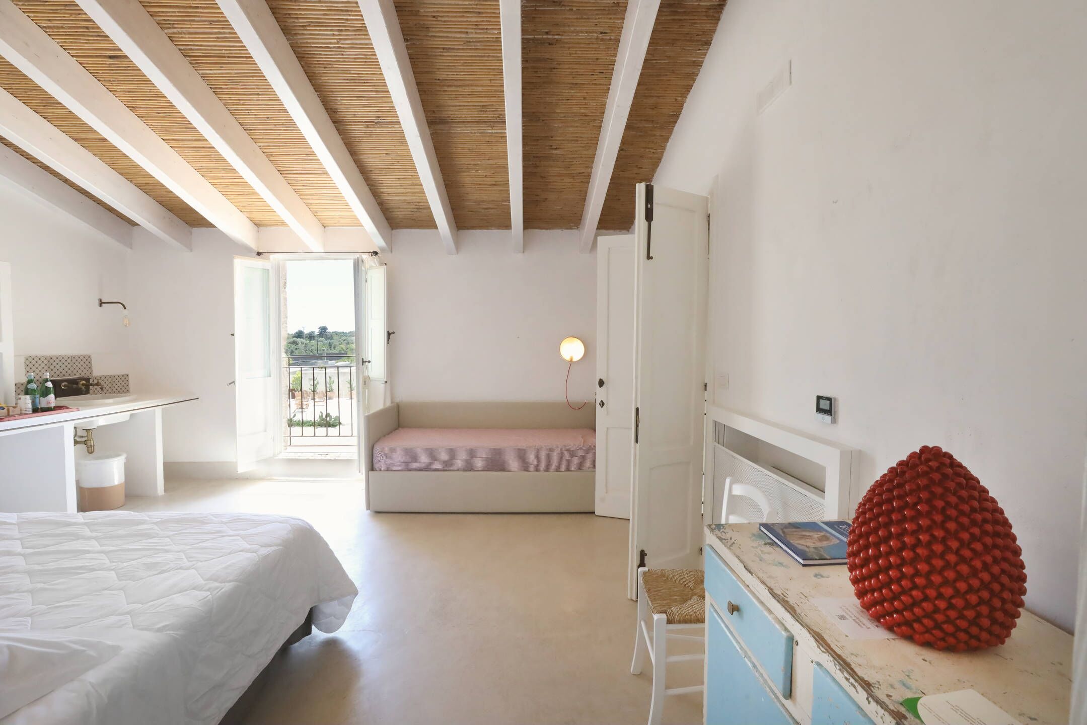 A bedroom with a bed, a desk, a bench, and a large red spherical object.