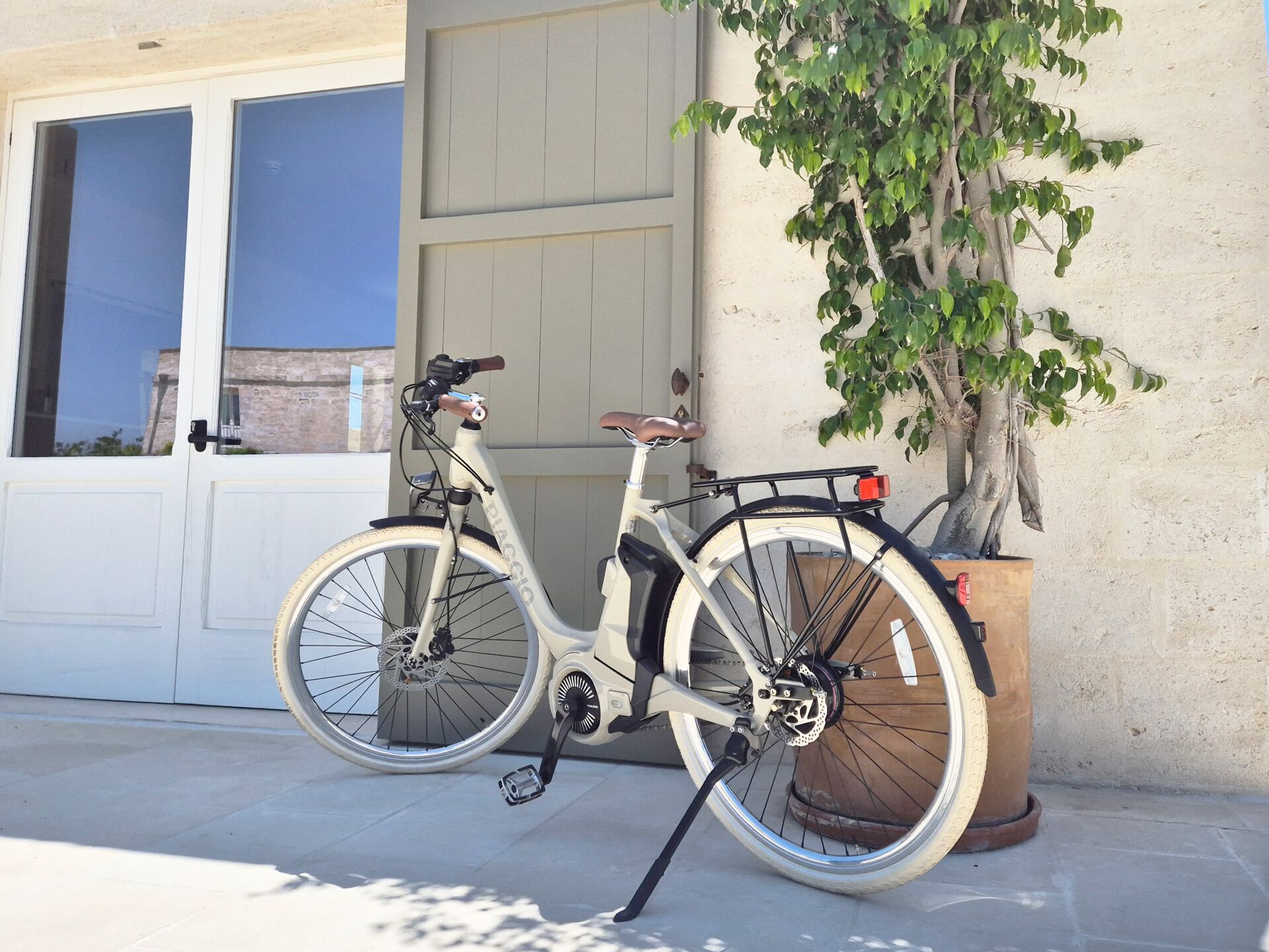 A white bicycle parked next to a building with a large tree and a garage door.