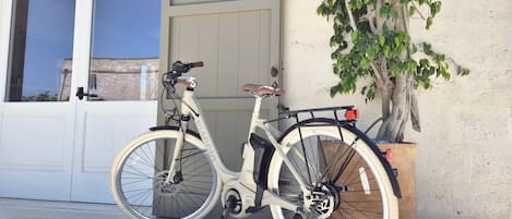 A white bicycle parked next to a building with a large tree and a garage door.