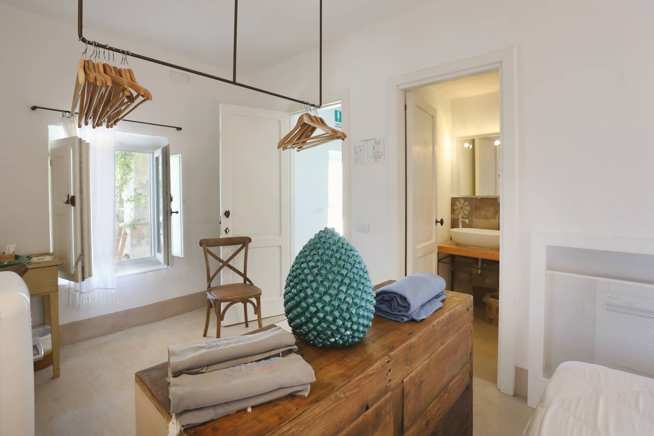 Une chambre avec une commode en bois, une chaise, un portant à vêtements et une vue sur la salle de bain.