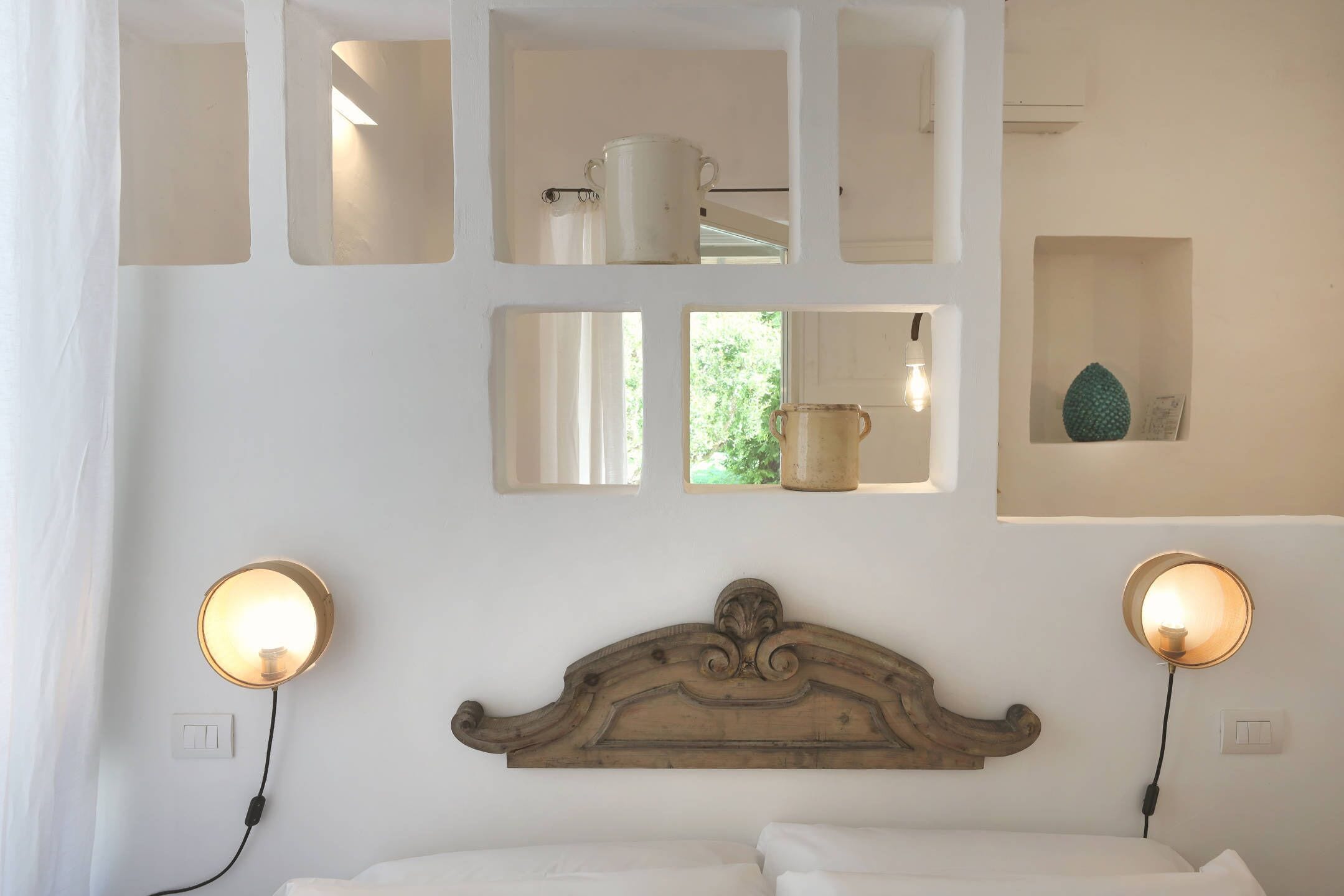 A bedroom with a wooden headboard, bedside lamps, a mirror, and a shelf with a vase.