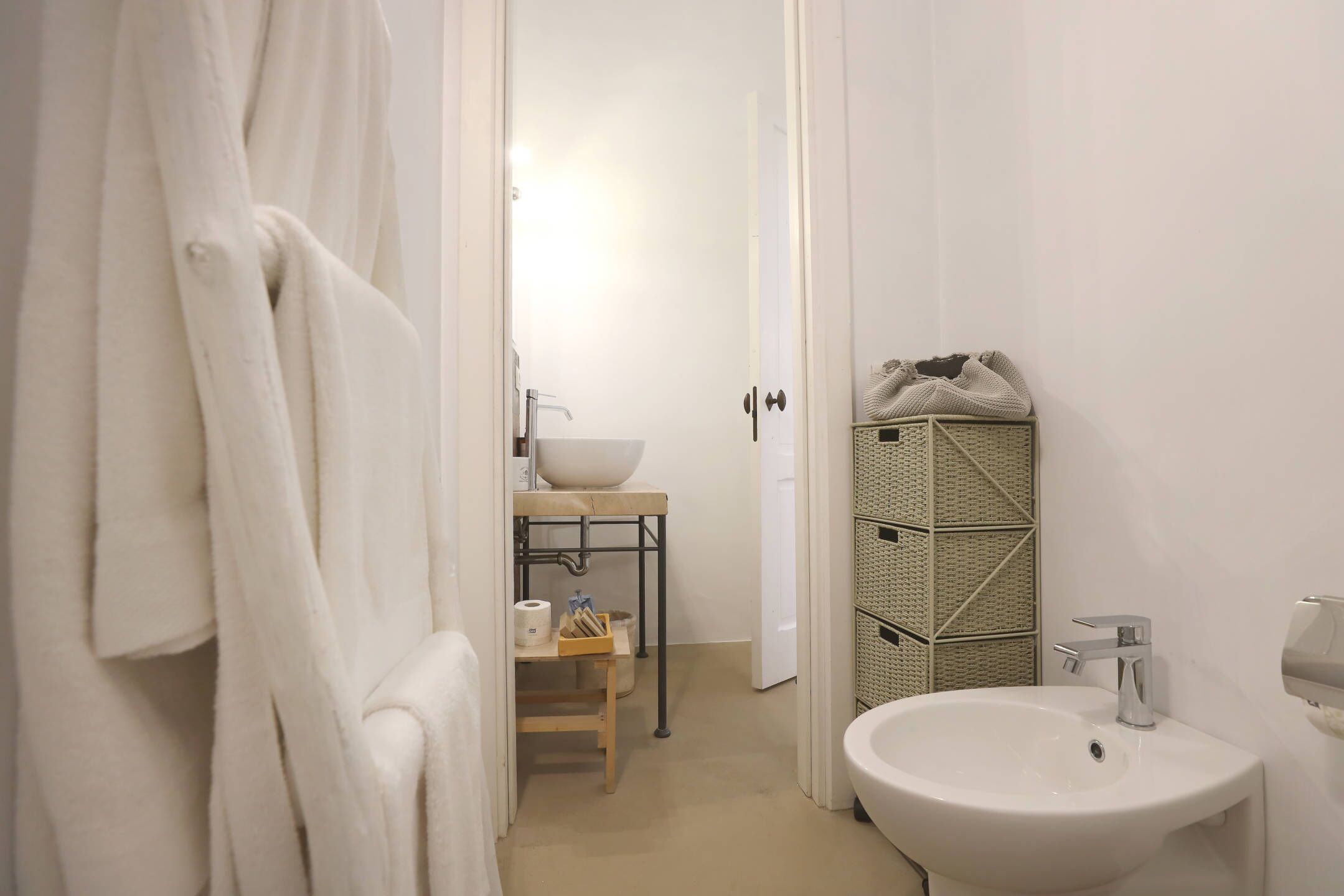 A bathroom with a white sink, a towel rack, and a shelf with toiletries.