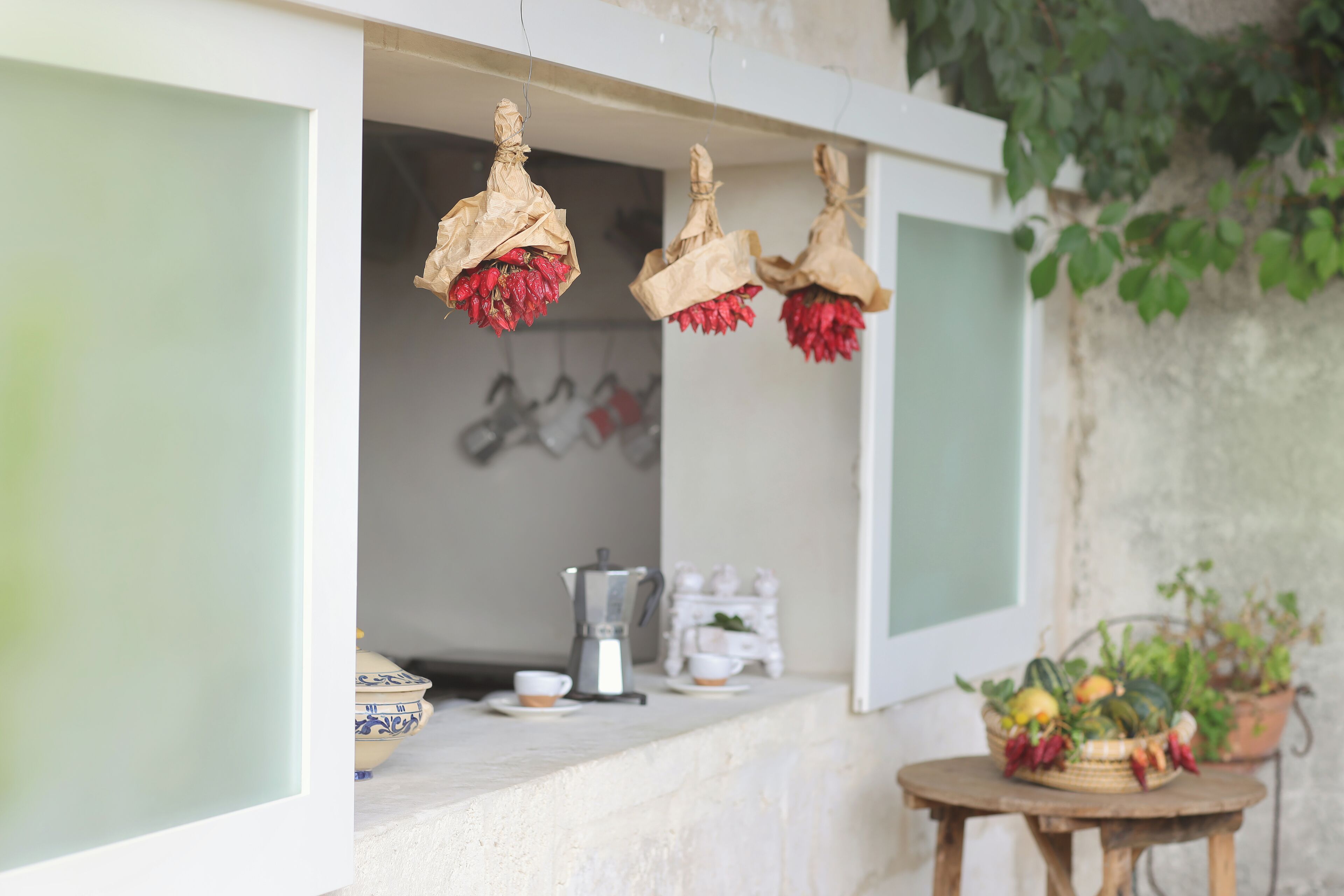 A kitchen with hanging paper decorations, a coffee maker, and a small table with a basket of fruits.
