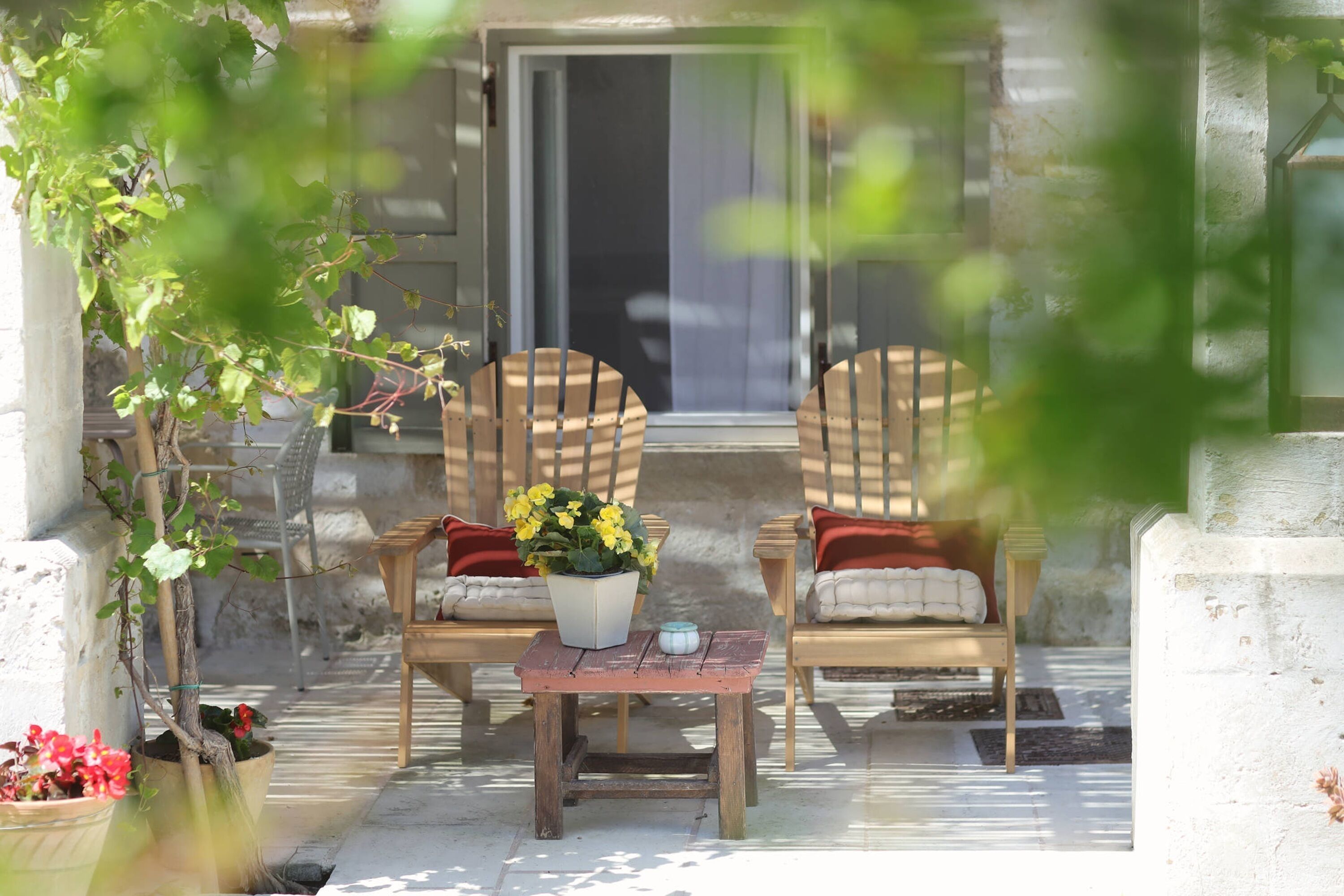 A patio with two wooden chairs, a small table, and a potted plant with yellow flowers.