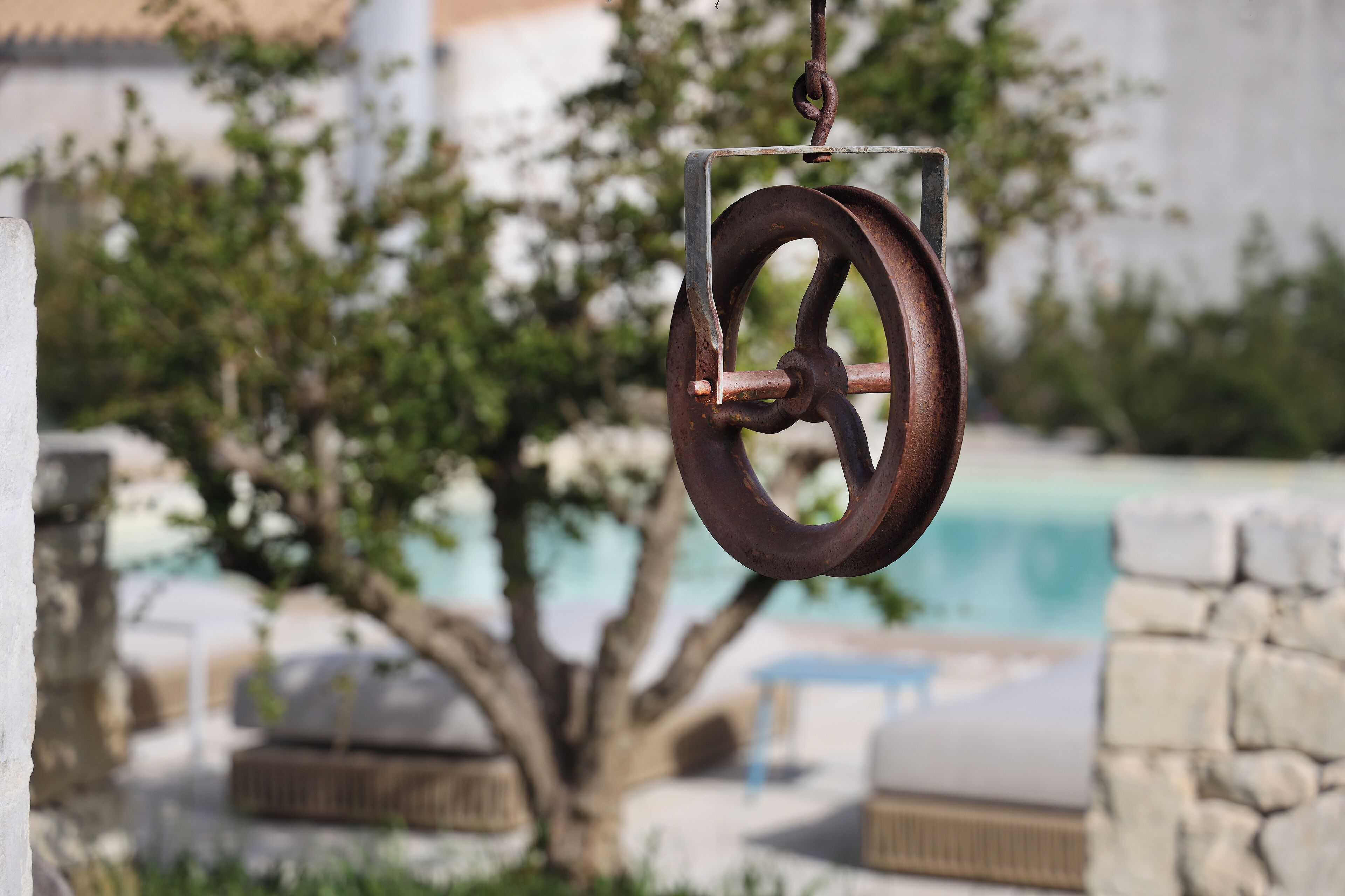 A rusty pulley system with a clear view of a pool and stone structures in the background.