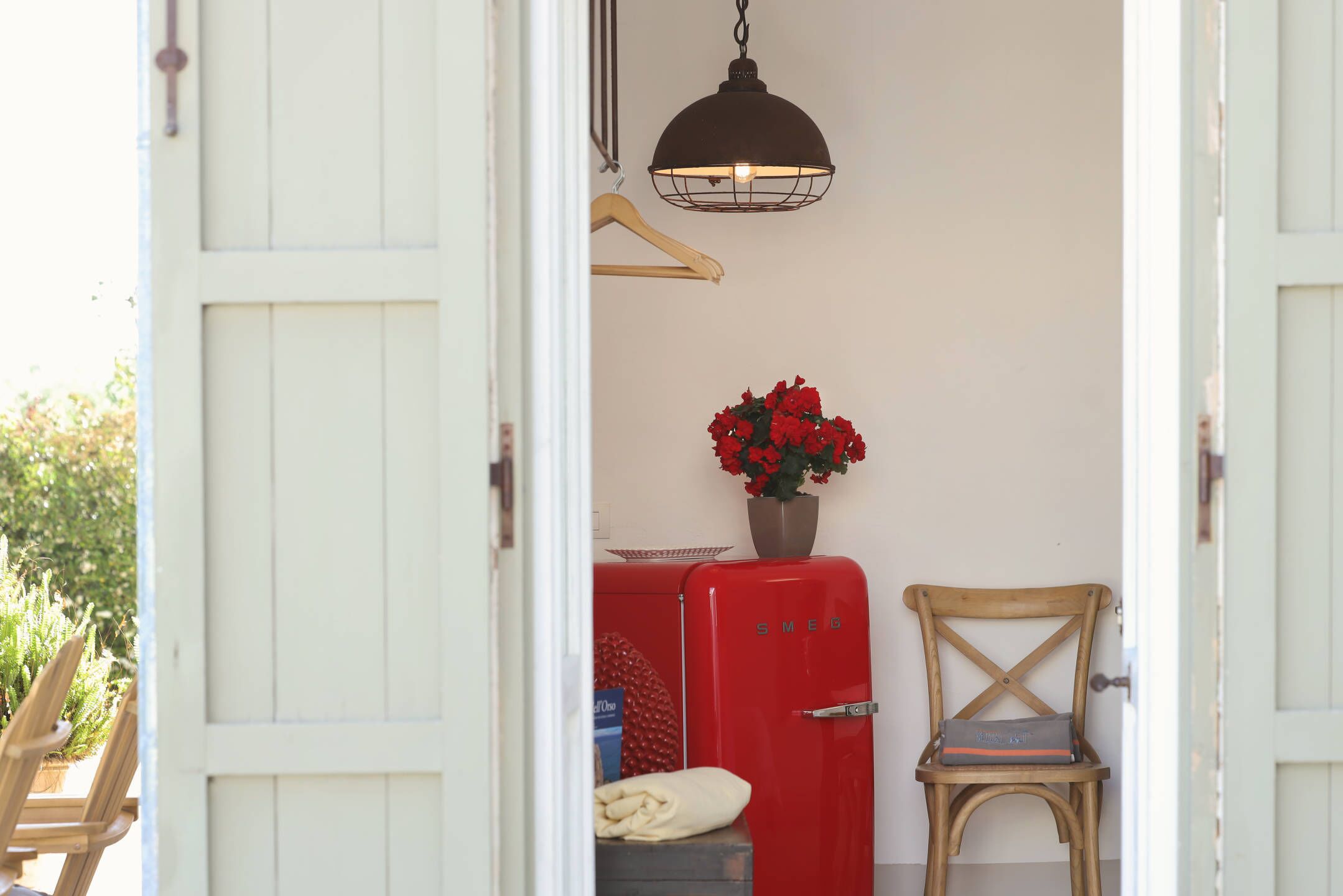 A doorway with a red vintage refrigerator, a wooden chair, and a hanging light fixture.