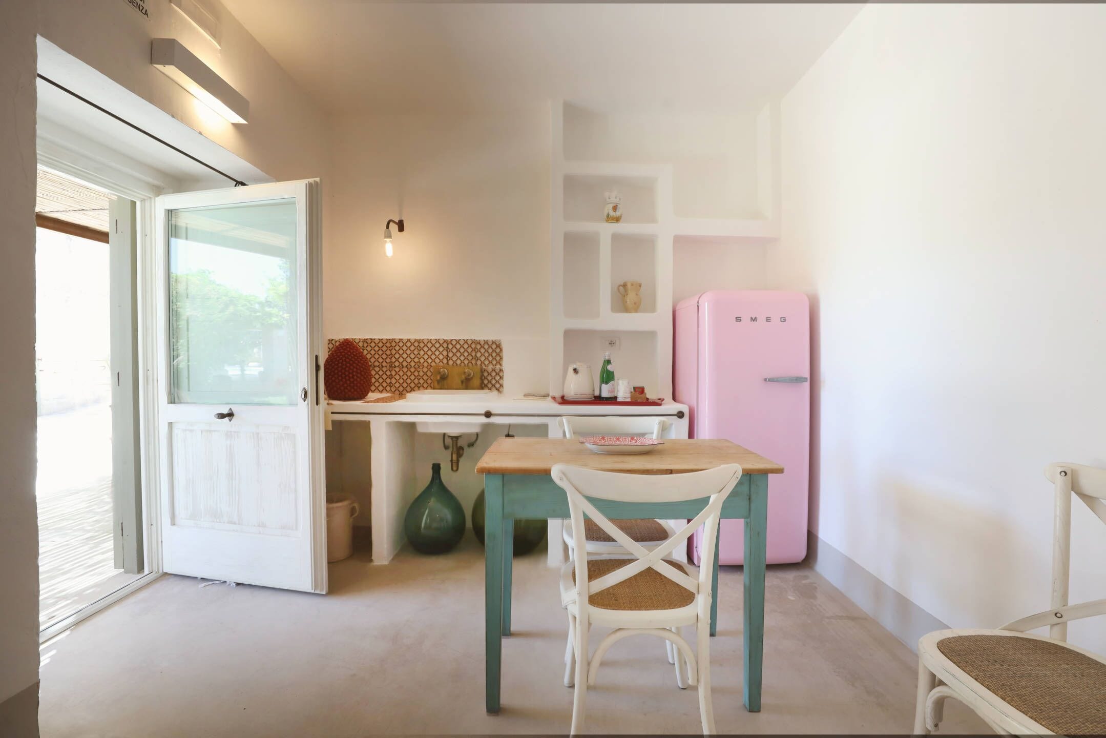 A kitchen with a white door, a pink refrigerator, a wooden table, and a white chair.