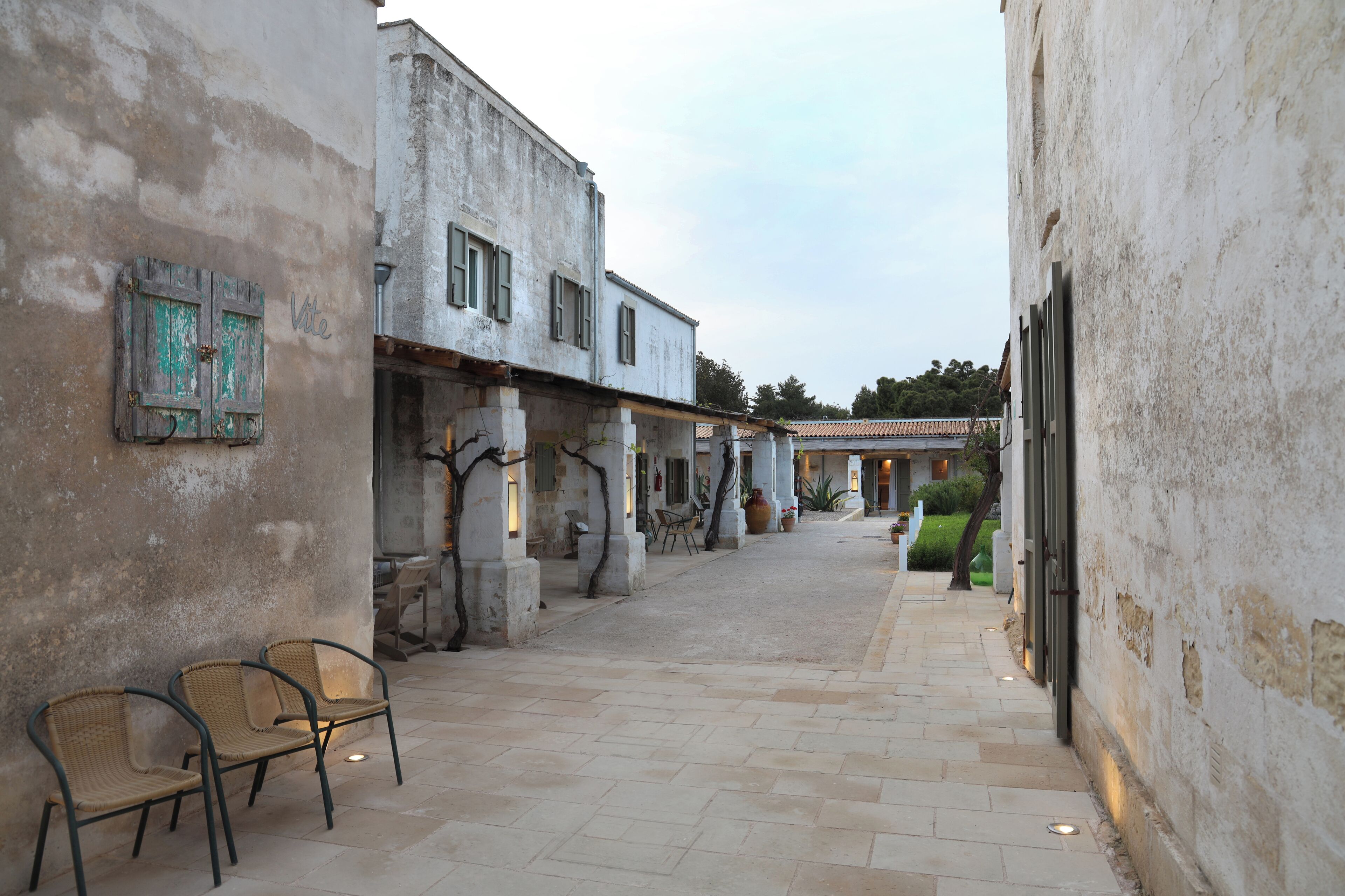 A narrow alleyway with rustic buildings, a few chairs, and a small table.