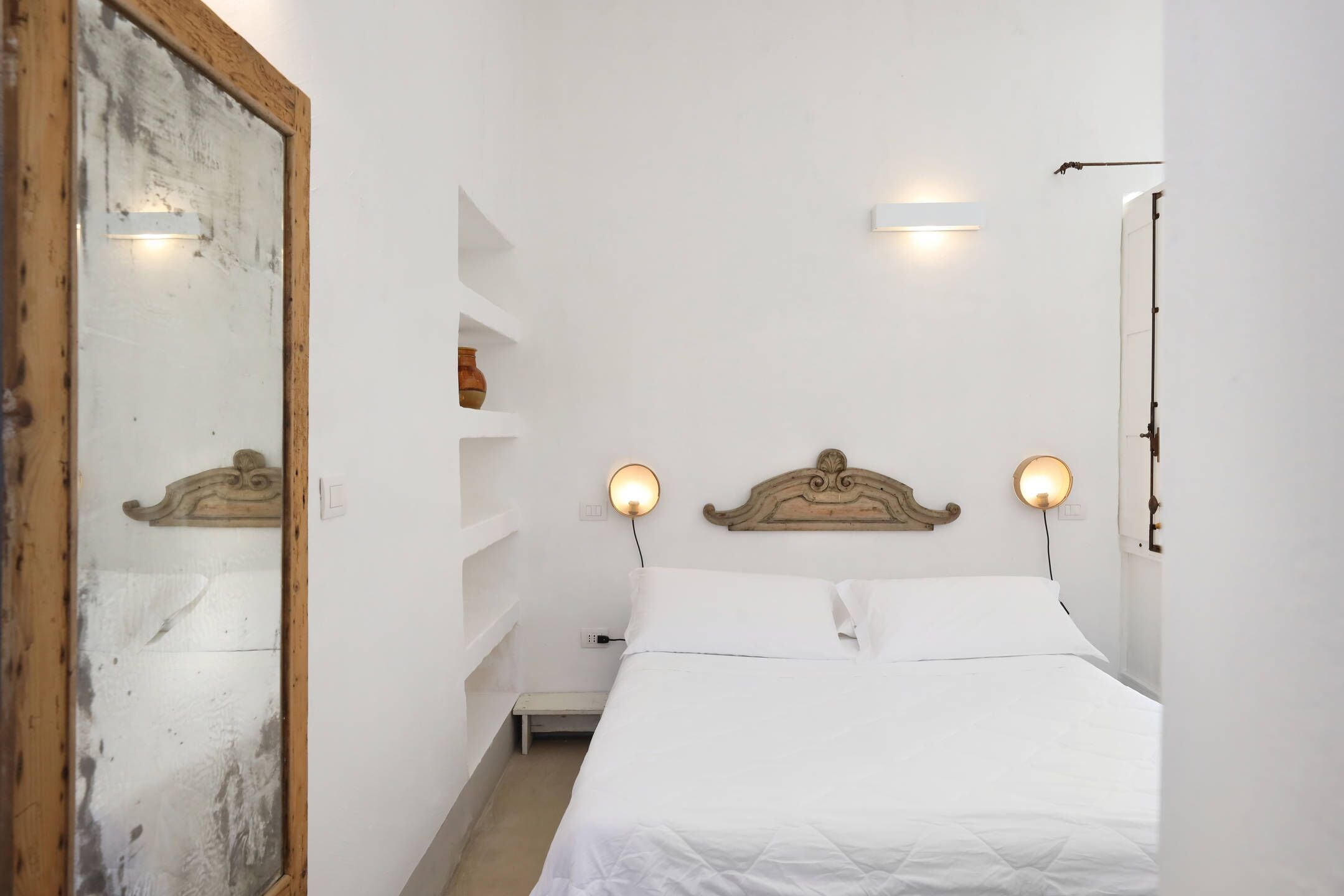 A bedroom with a bed, bedside tables, wall-mounted shelves, and a mirror.