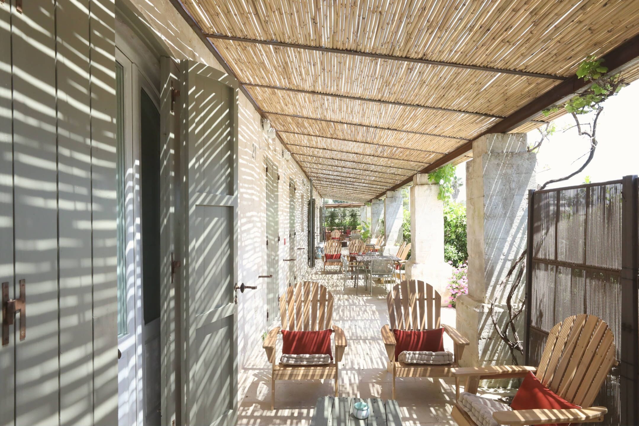 A covered outdoor seating area with wooden chairs and tables, a concrete pillar, and a bamboo ceiling.
