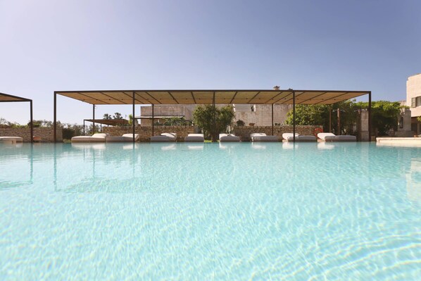 A clear swimming pool with lounge chairs and a covered seating area. - Masseria Borgo Sentinella (Melendugno)