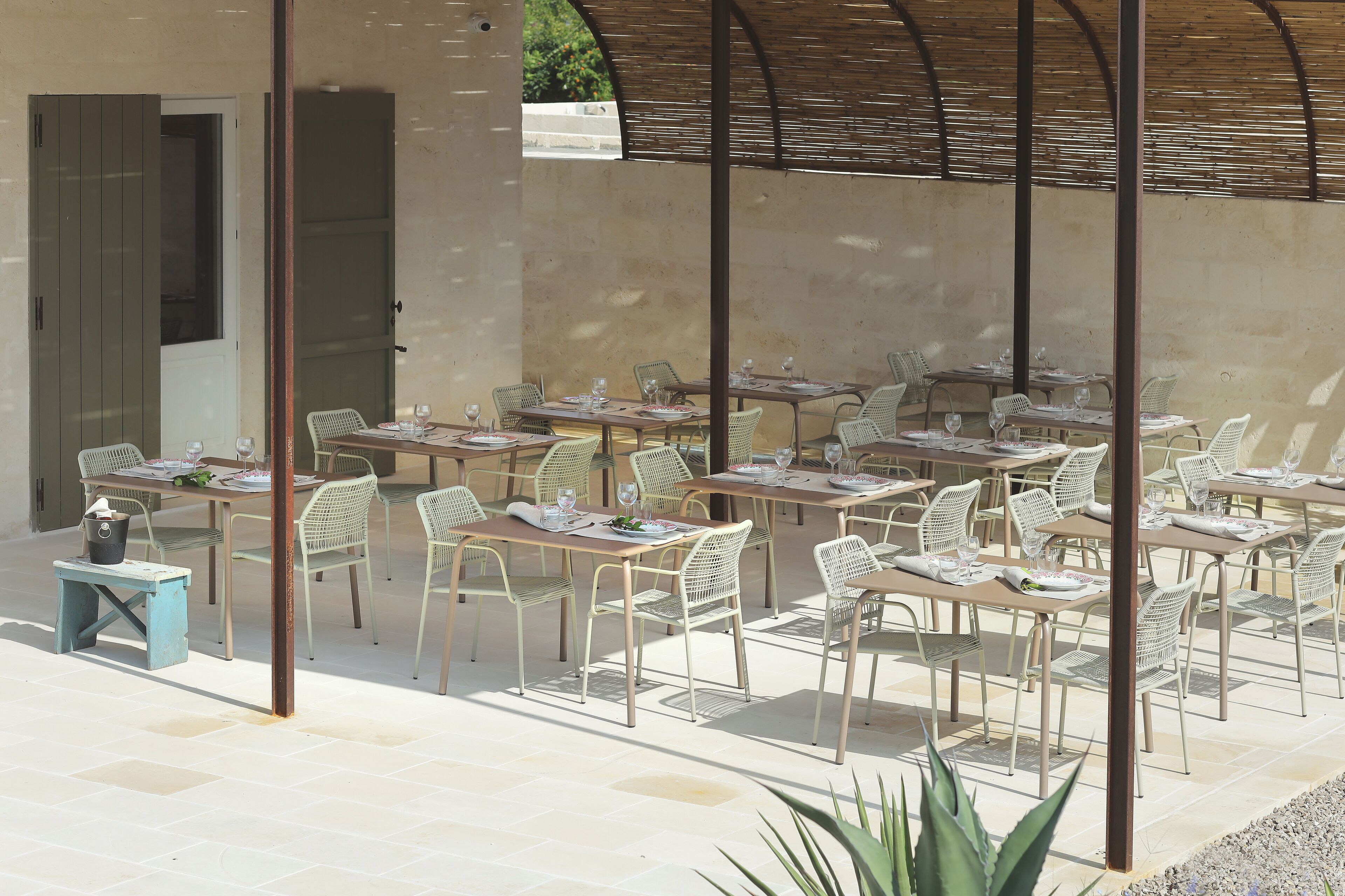 Een terras met meerdere tafels en stoelen, een overdekt gedeelte en een stenen muur.