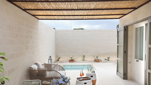 Ein Patio mit Pool, Korbmöbeln und Topfpflanzen.