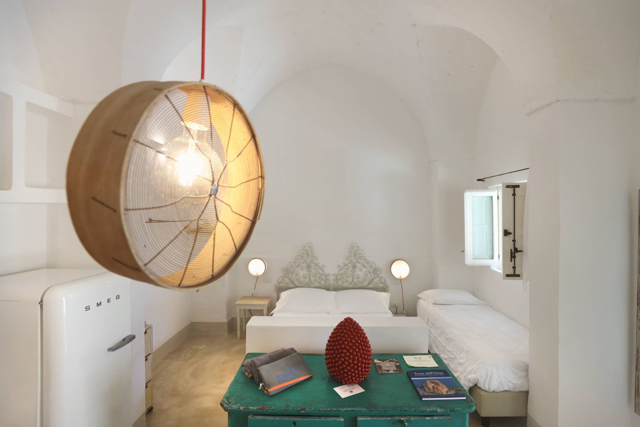 Une chambre à coucher comprenant un lit, des tables de chevet, un luminaire suspendu et une petite table sur laquelle sont posés des livres et un objet décoratif.