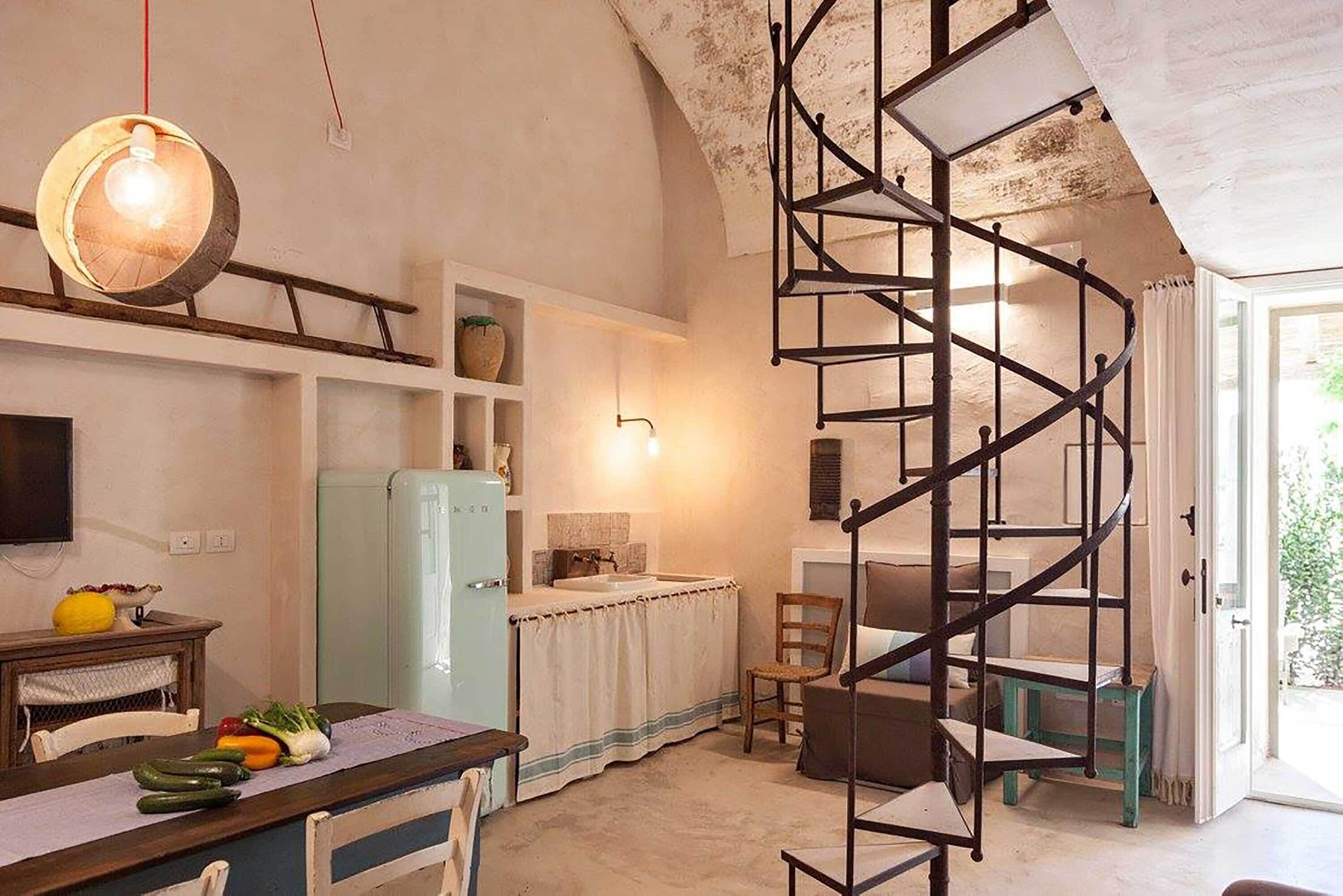 Une cuisine compacte avec un escalier en colimaçon, un coin repas avec une table dressée pour deux personnes et un réfrigérateur.