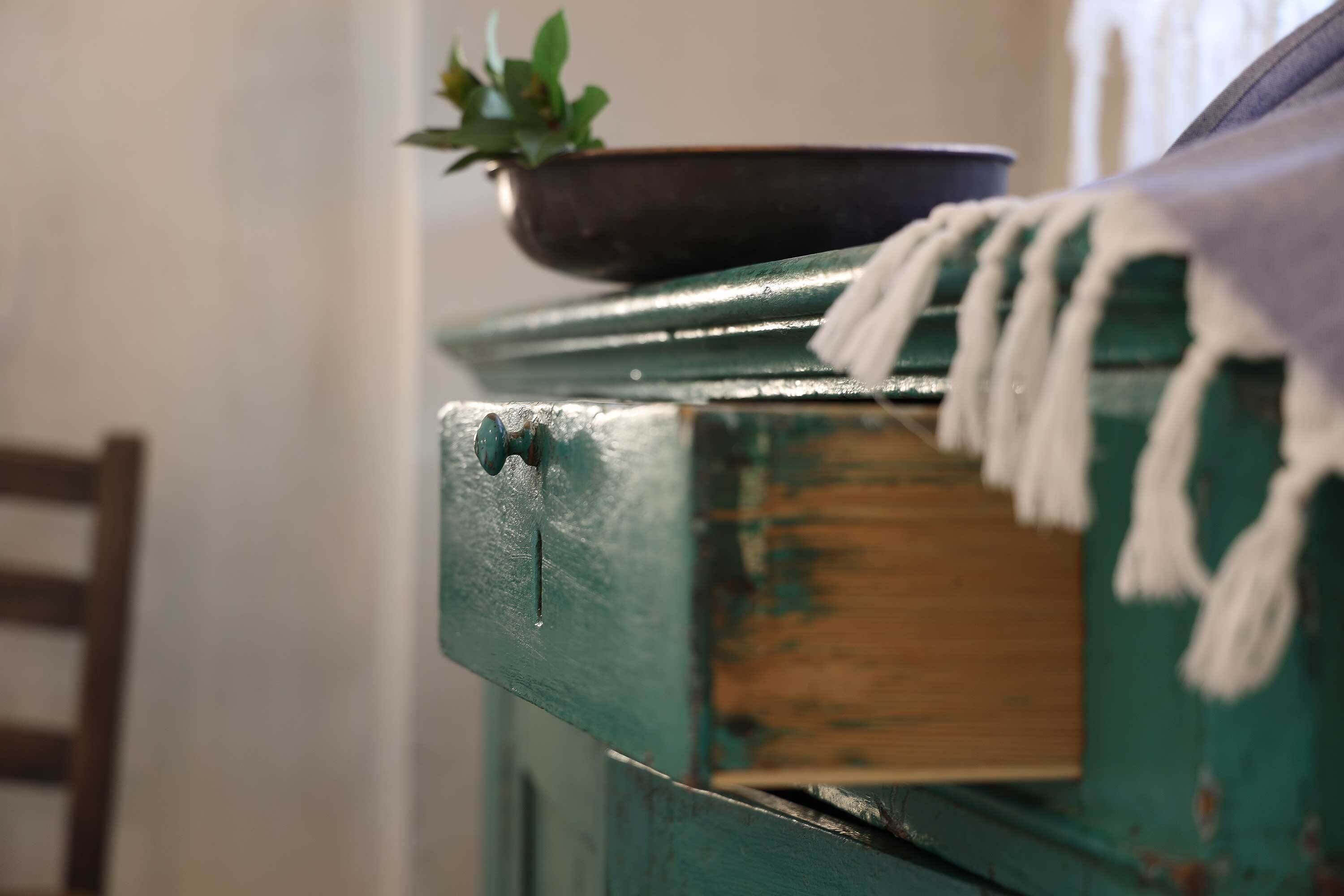Primer plano de un mueble de madera verde con una planta en una maceta negra y un paño blanco cubriéndolo.