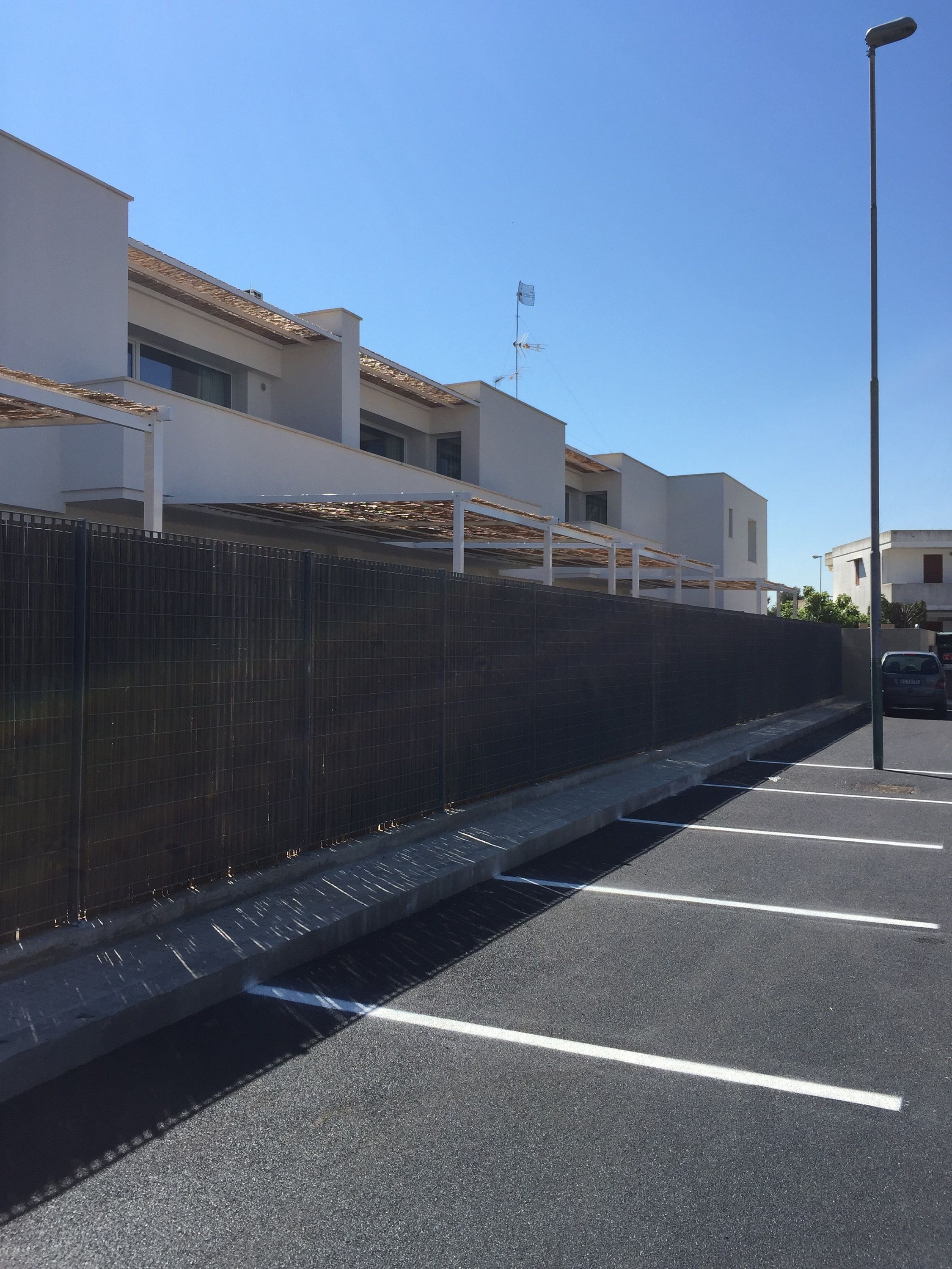 Un espace de stationnement avec des places délimitées, une clôture et, au fond, un bâtiment doté d’un toit plat.
