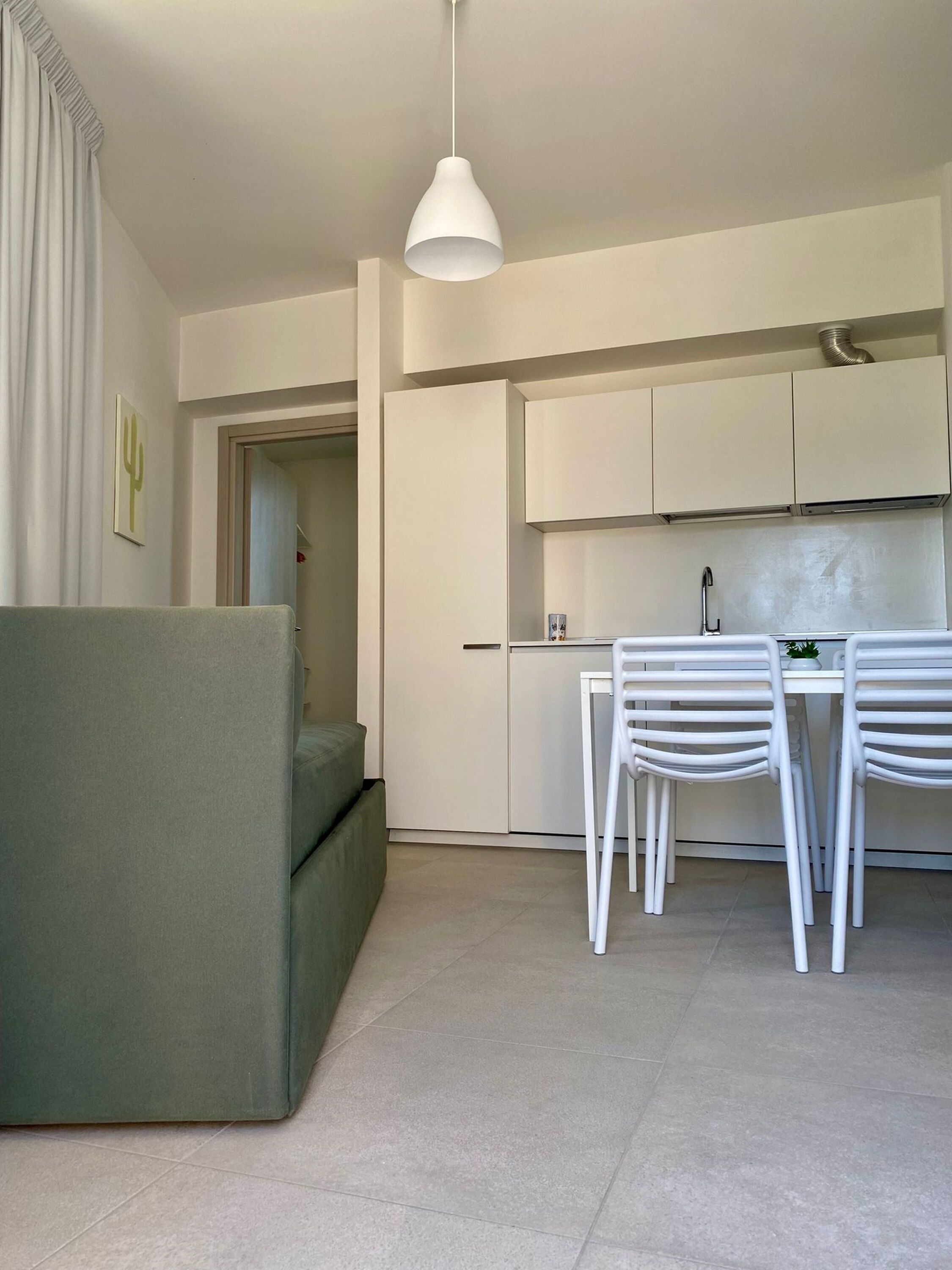 Une cuisine moderne avec des meubles blancs, une table à manger avec des chaises et un luminaire suspendu.