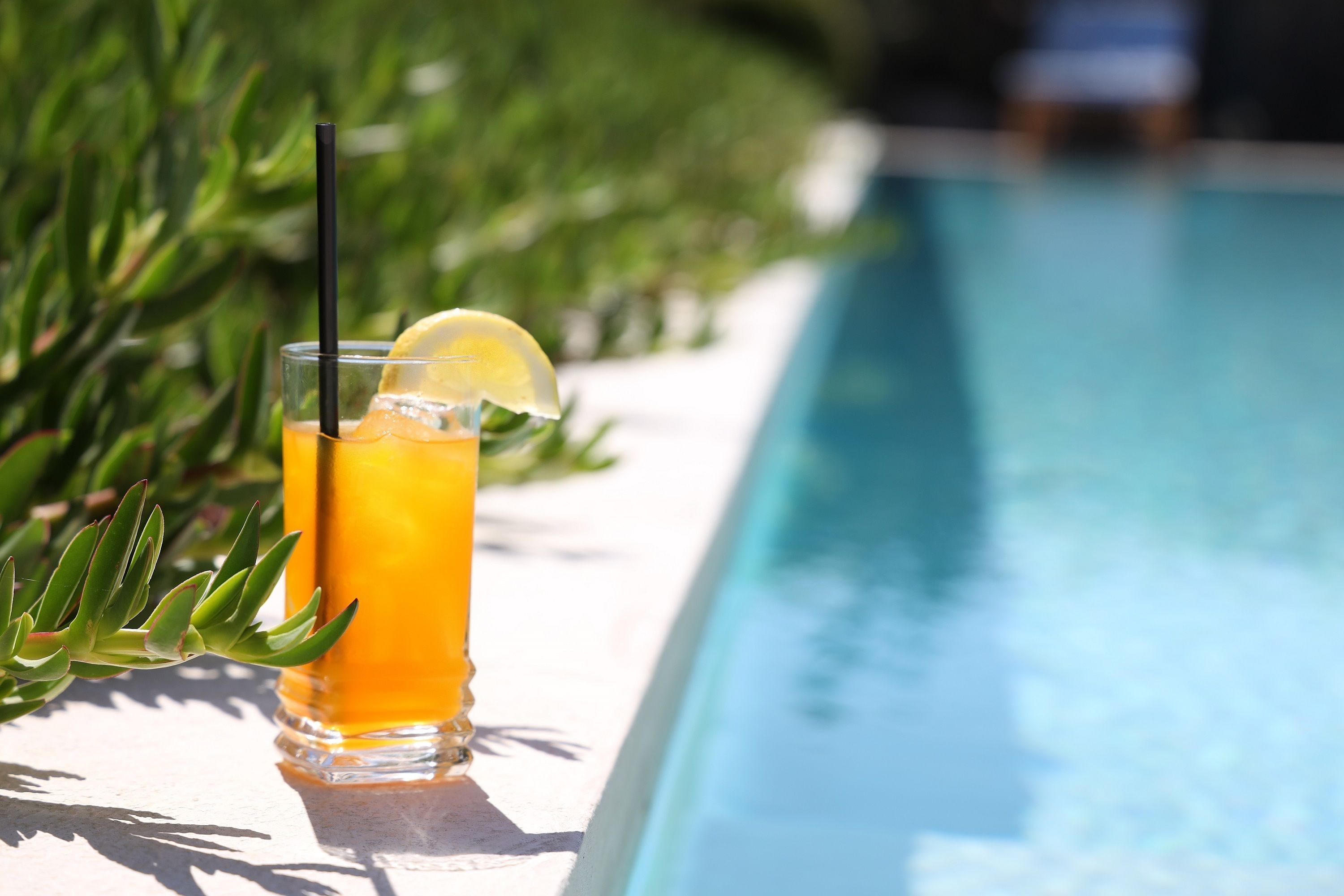 Un vaso de jugo de naranja con una rodaja de limón y una pajita junto a una piscina.