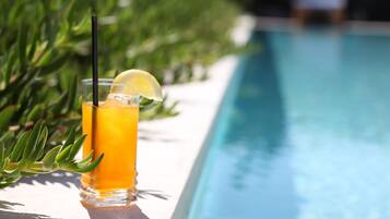 A glass of orange beverage with a lemon wedge and straw by a poolside.