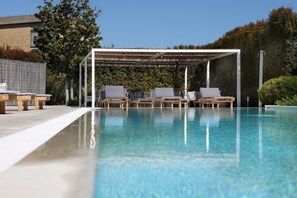 Una piscina cristalina con sillas de descanso y una zona de estar cubierta.