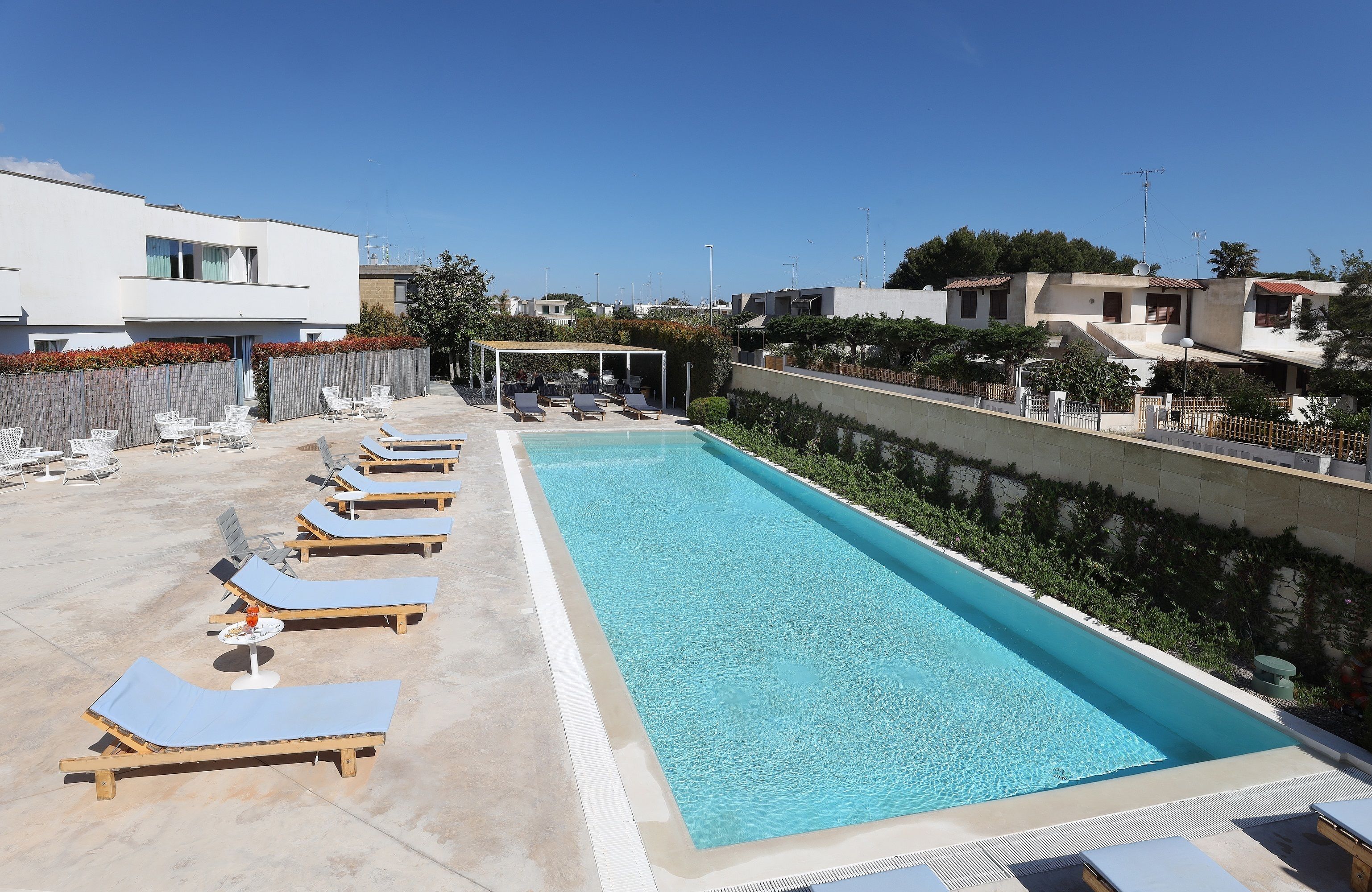 A rectangular swimming pool with lounge chairs and umbrellas, surrounded by a low wall and vegetation.