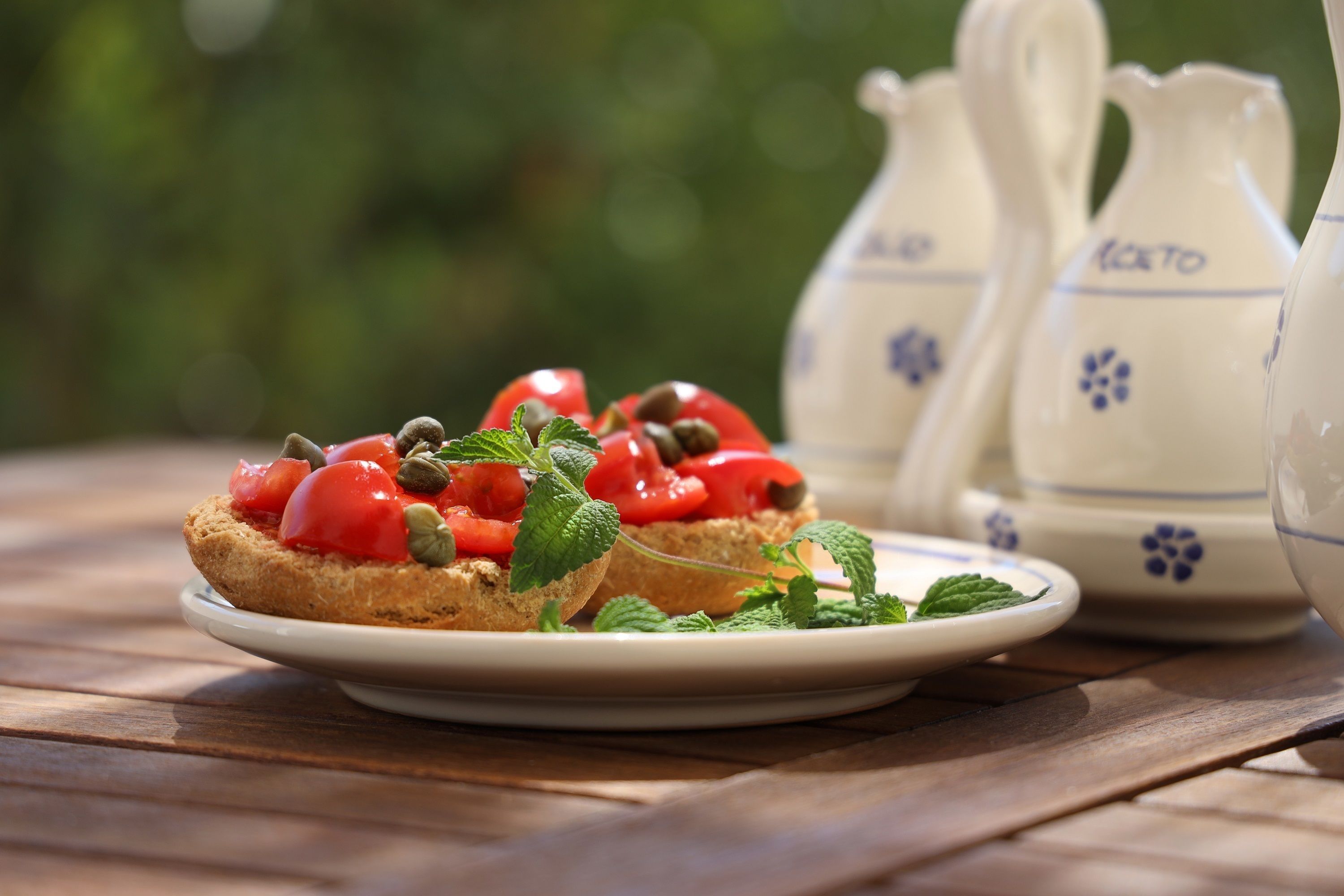 Un plato con un sándwich cubierto de tomates y hojas de menta, acompañado de dos jarras con diseños florales.