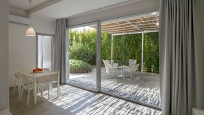 A modern room with a sliding glass door leading to an outdoor patio. The room has a dining table with chairs and a small table with a bowl of fruit. - Salento Residence & Suite (Lecce)