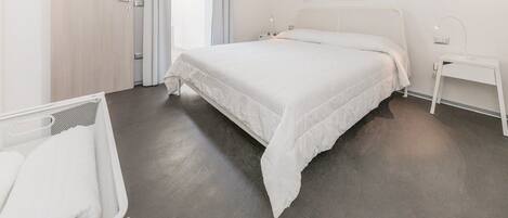 Une chambre d’hôtel moderne avec un grand lit, une table de chevet, un petit bureau et une fenêtre avec des rideaux.
