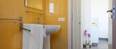 Un baño con baldosas amarillas, un lavamanos blanco, un perchero para toallas y una mampara de cristal.