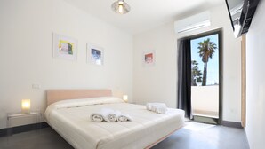 A modern hotel room with a large bed, bedside tables, and a view of palm trees through the window. - Salento Residence & Suite (Lecce)