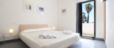 Een moderne hotelkamer met een groot bed, nachtkastjes en uitzicht op palmbomen door het raam.