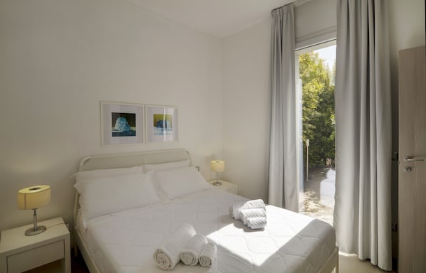 Habitación de hotel con cama, dos lámparas de noche, una ventana con cortinas y una puerta.
