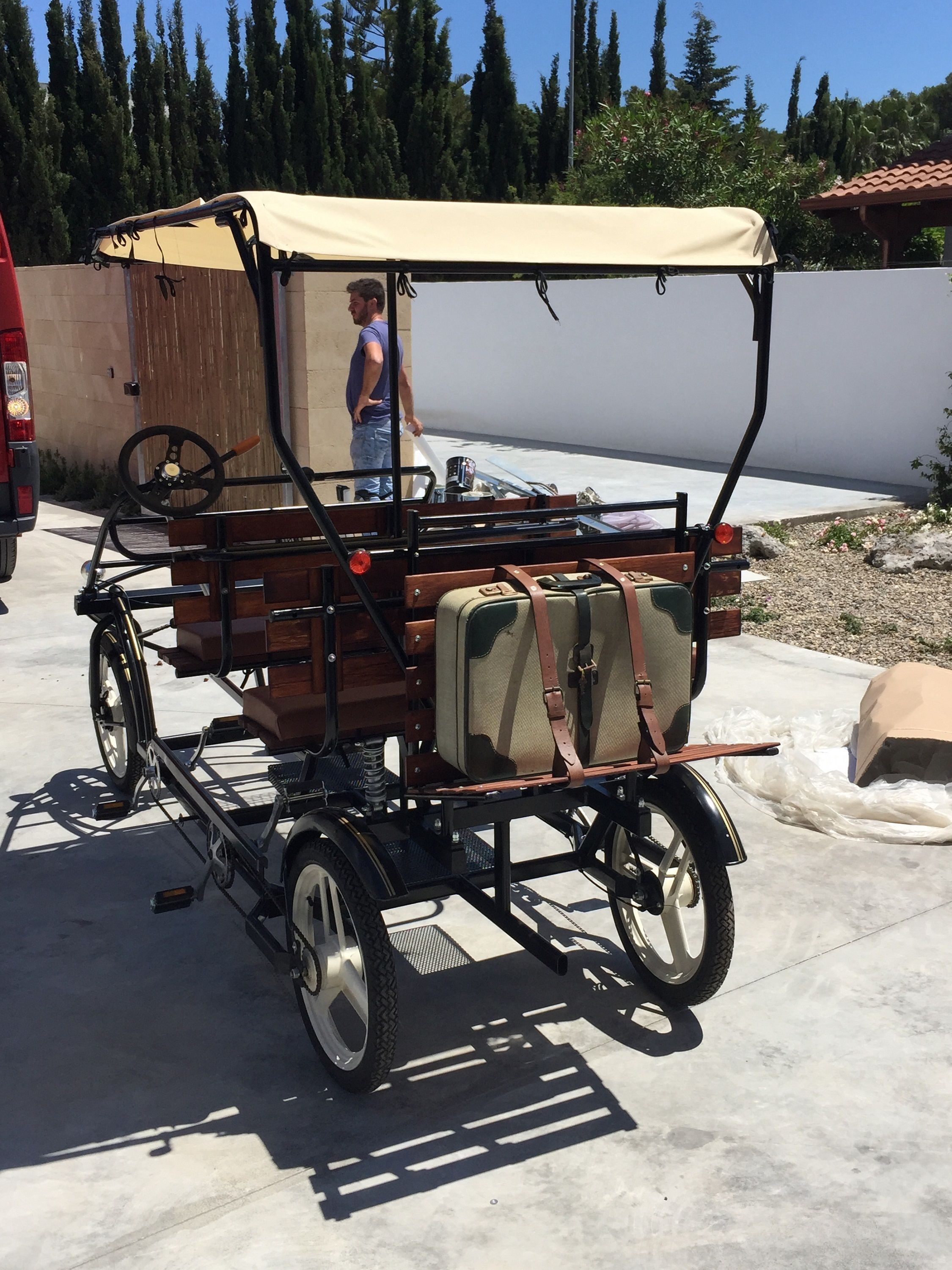 A vintage-style cart with a canvas cover, equipped with a steering wheel and storage compartments, parked outdoors.