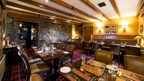 A restaurant with wooden beams, stone walls, and plaid tablecloths. Tables are set with plates, glasses, and cutlery.