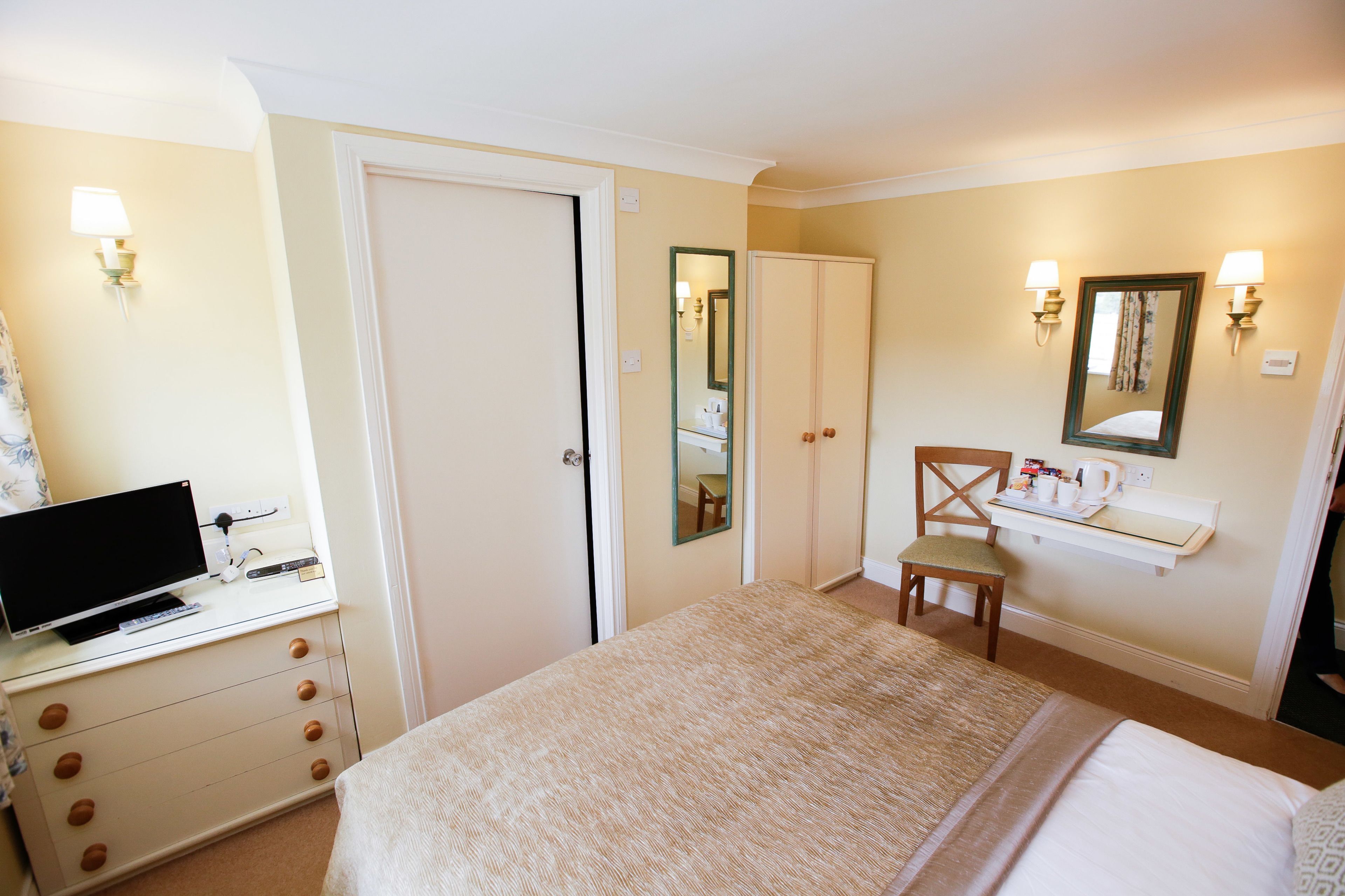 Habitación de hotel con cama, escritorio con ordenador, silla, espejo y baño pequeño.