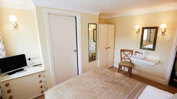 Quarto de hotel com cama, escrivaninha com computador, cadeira, espelho e um pequeno banheiro.