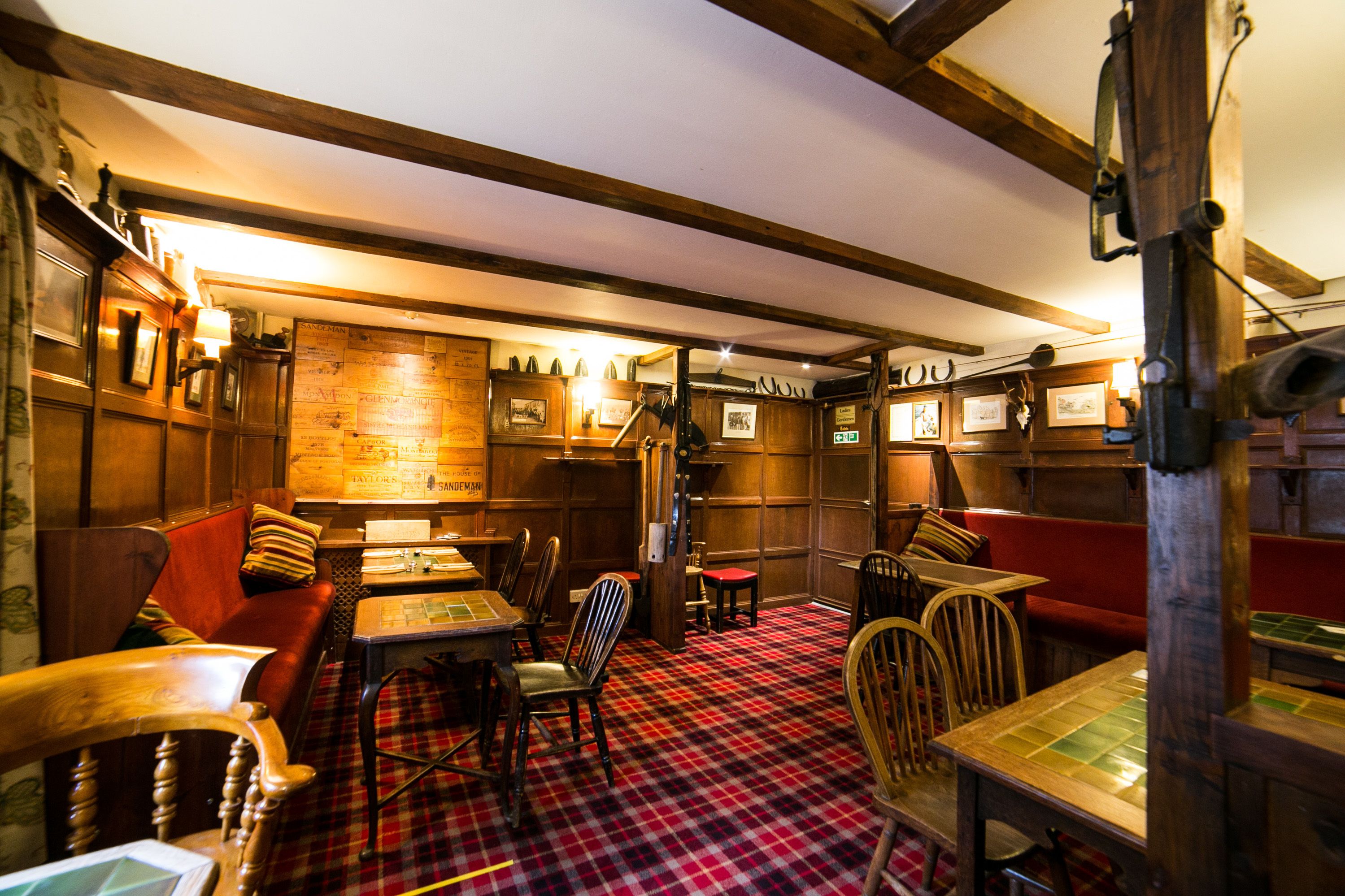A traditional pub interior with wooden beams, red and black checkered flooring, and a variety of seating including tables and benches.