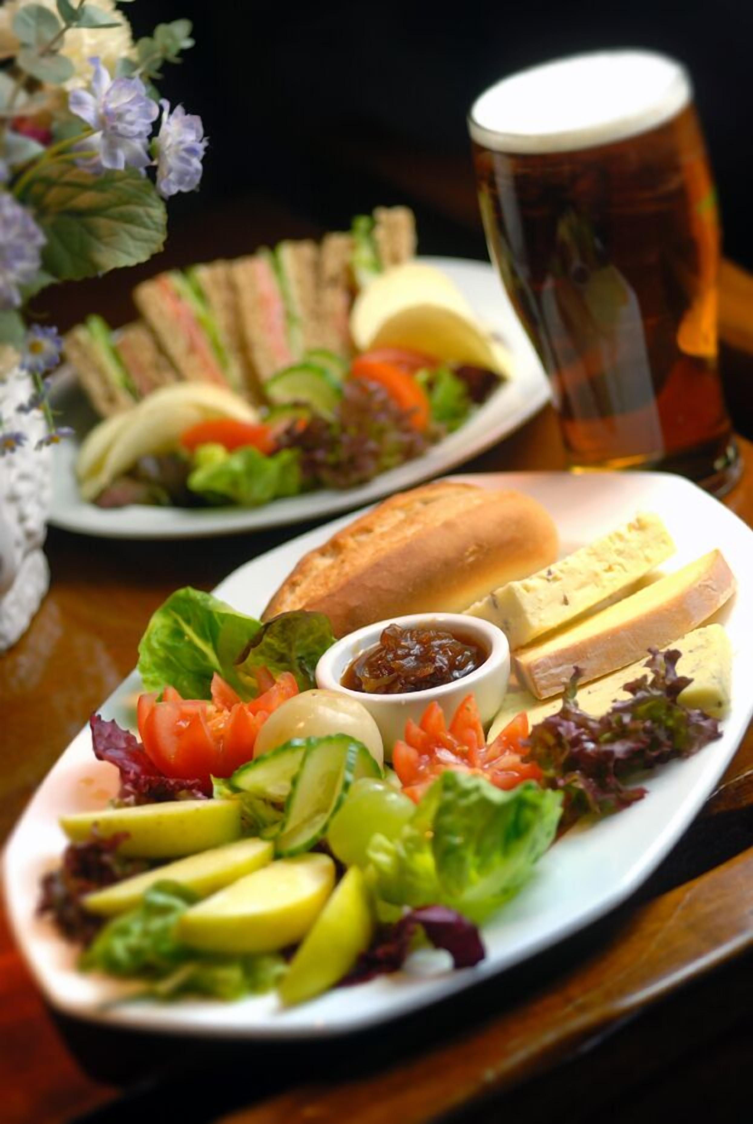 Eine Mahlzeit mit Sandwiches, Salat, Käse und einem Glas Bier auf einer Holztischplatte.