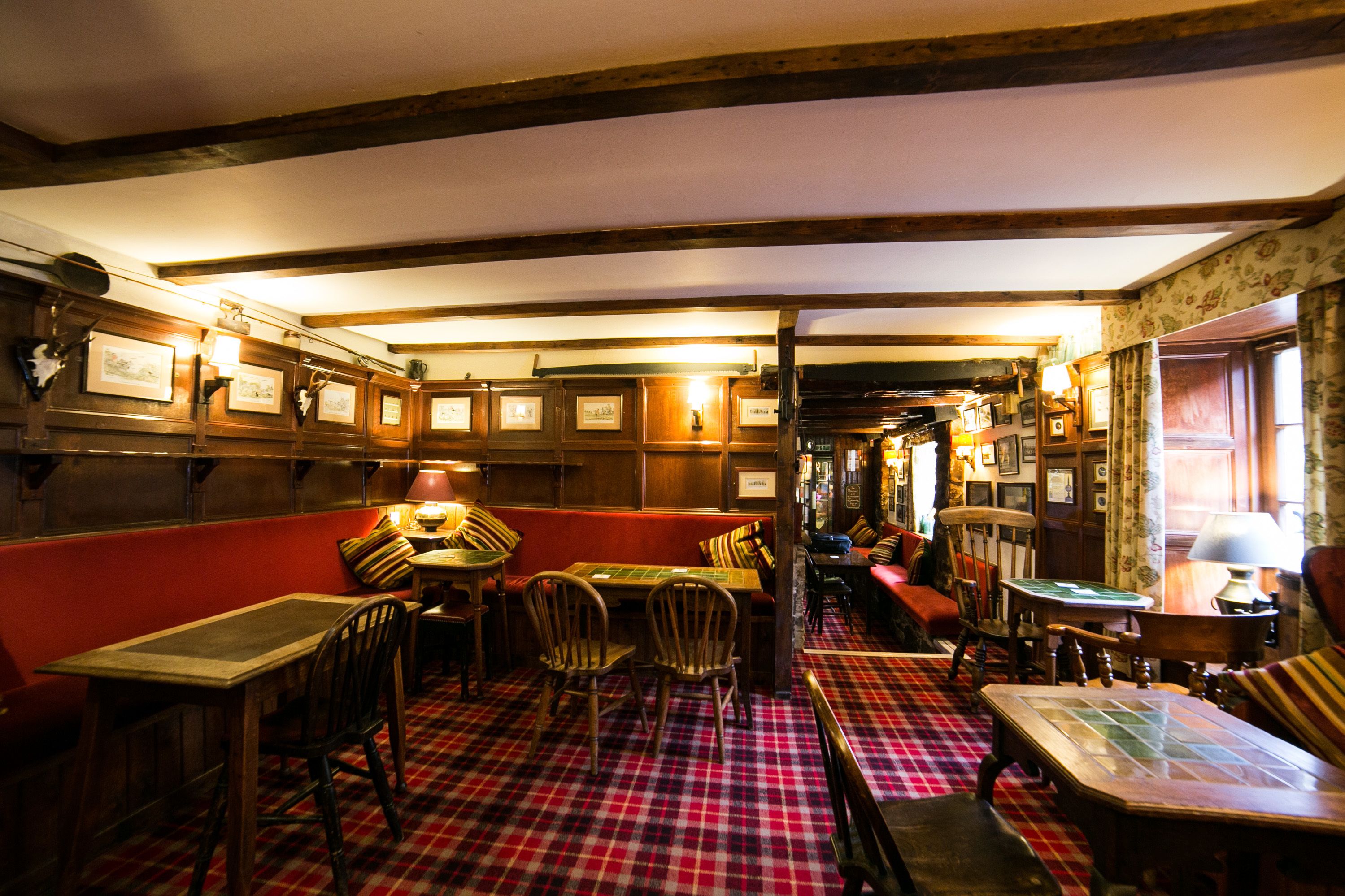 A cozy pub with wooden furniture, a red and black checkered floor, and framed pictures on the walls.
