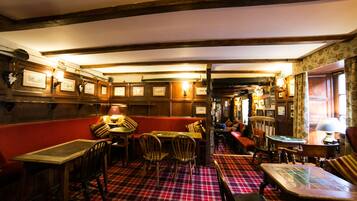 A cozy pub with wooden furniture, a red and black checkered floor, and framed pictures on the walls.