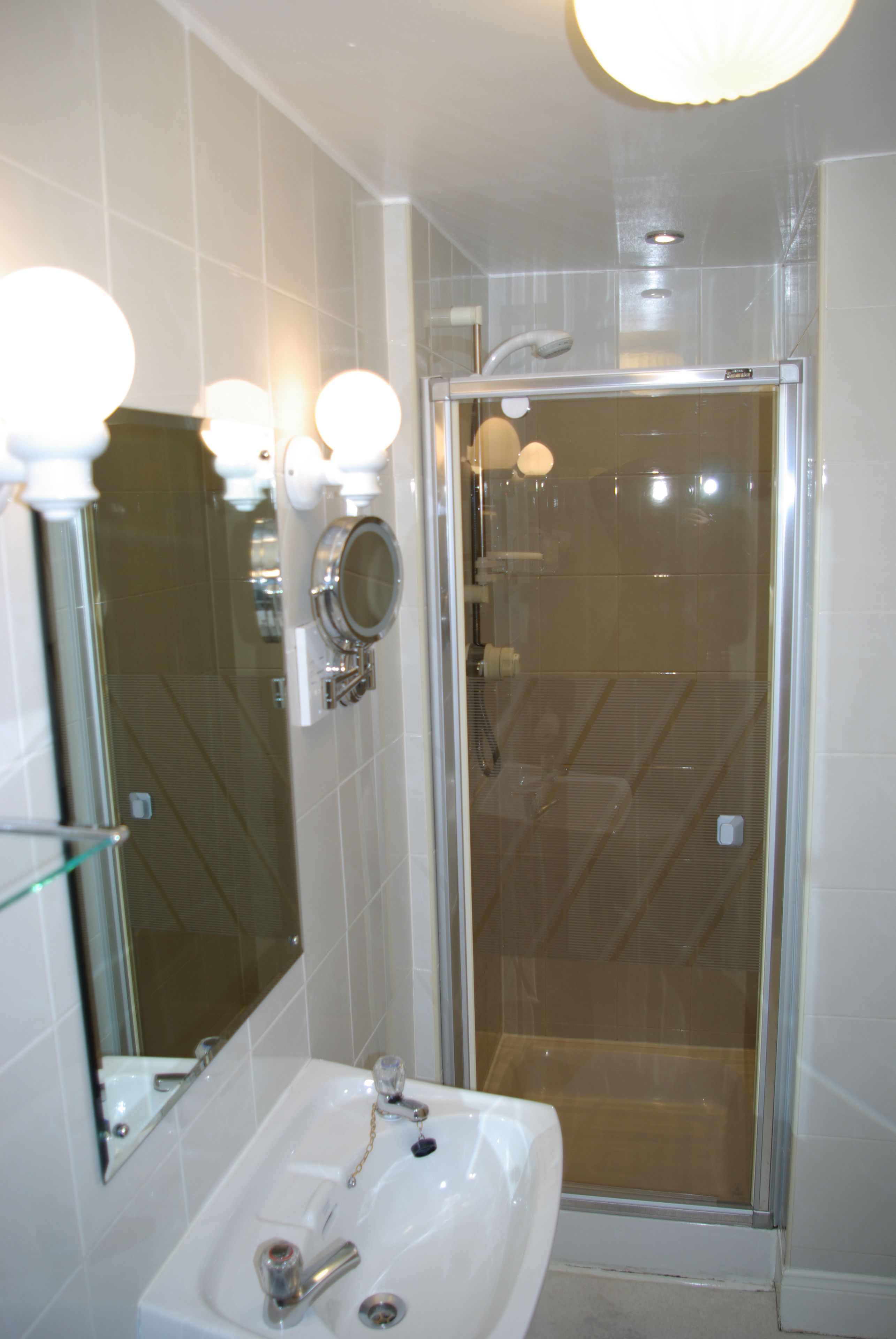 A bathroom with a glass-enclosed shower, a sink with a mirror, and a light fixture above the mirror.