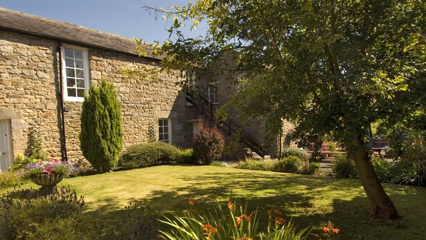 A stone building with a well-maintained garden, including a lawn, flower beds, and a variety of plants.