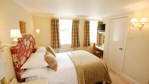 A hotel room with a bed, a desk, a chair, a television, and a door.