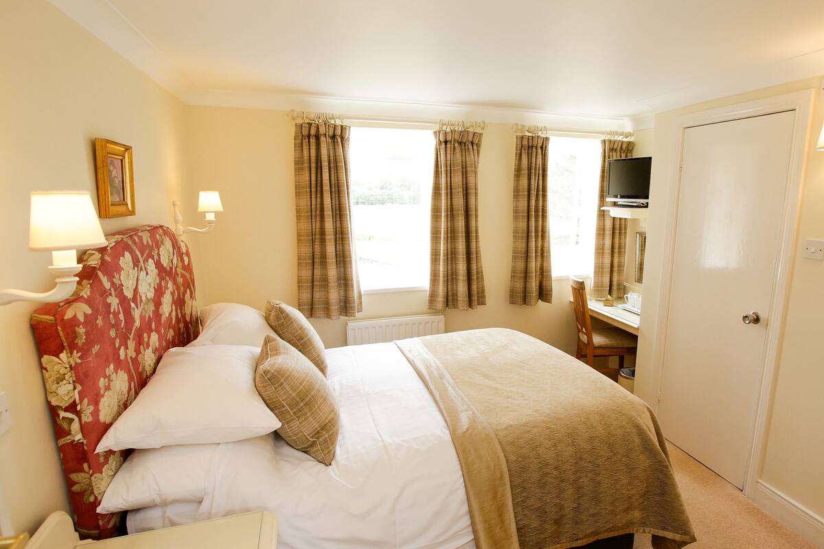 A hotel room with a bed, a desk, a chair, a television, and a door.
