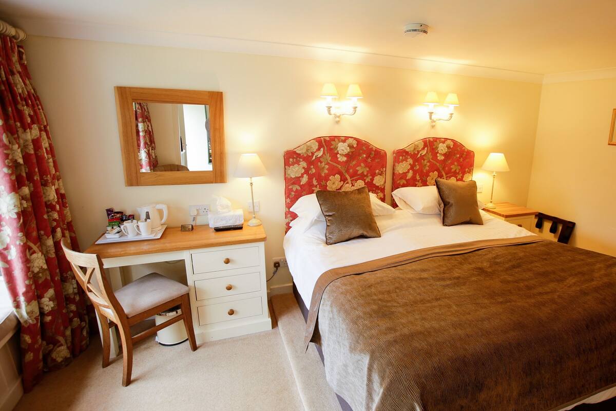 A hotel room with a bed, bedside lamps, a desk with a chair, a mirror, and a picture on the wall.