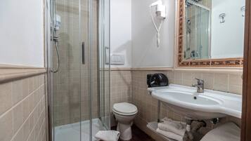 Casa de banho com chuveiro em compartimento de vidro, sanita branca, lavatório com espelho e toalhas no chão.