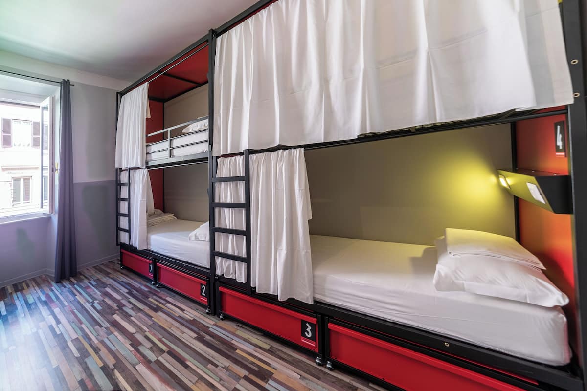 A room with bunk beds, a ladder, and a window with curtains.