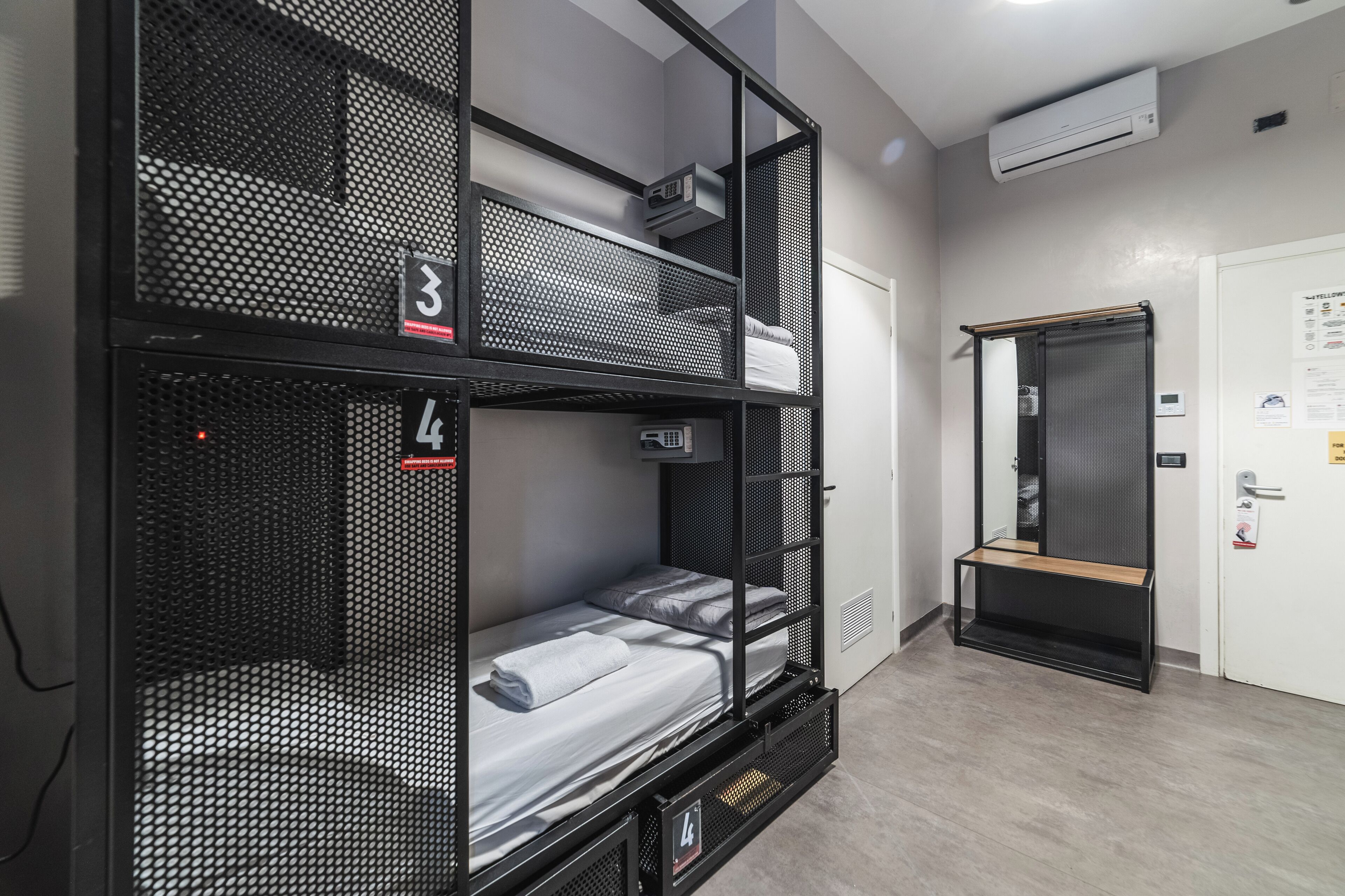 Habitación con literas, un cartel con un número, una mesita pequeña y una puerta con espejo.