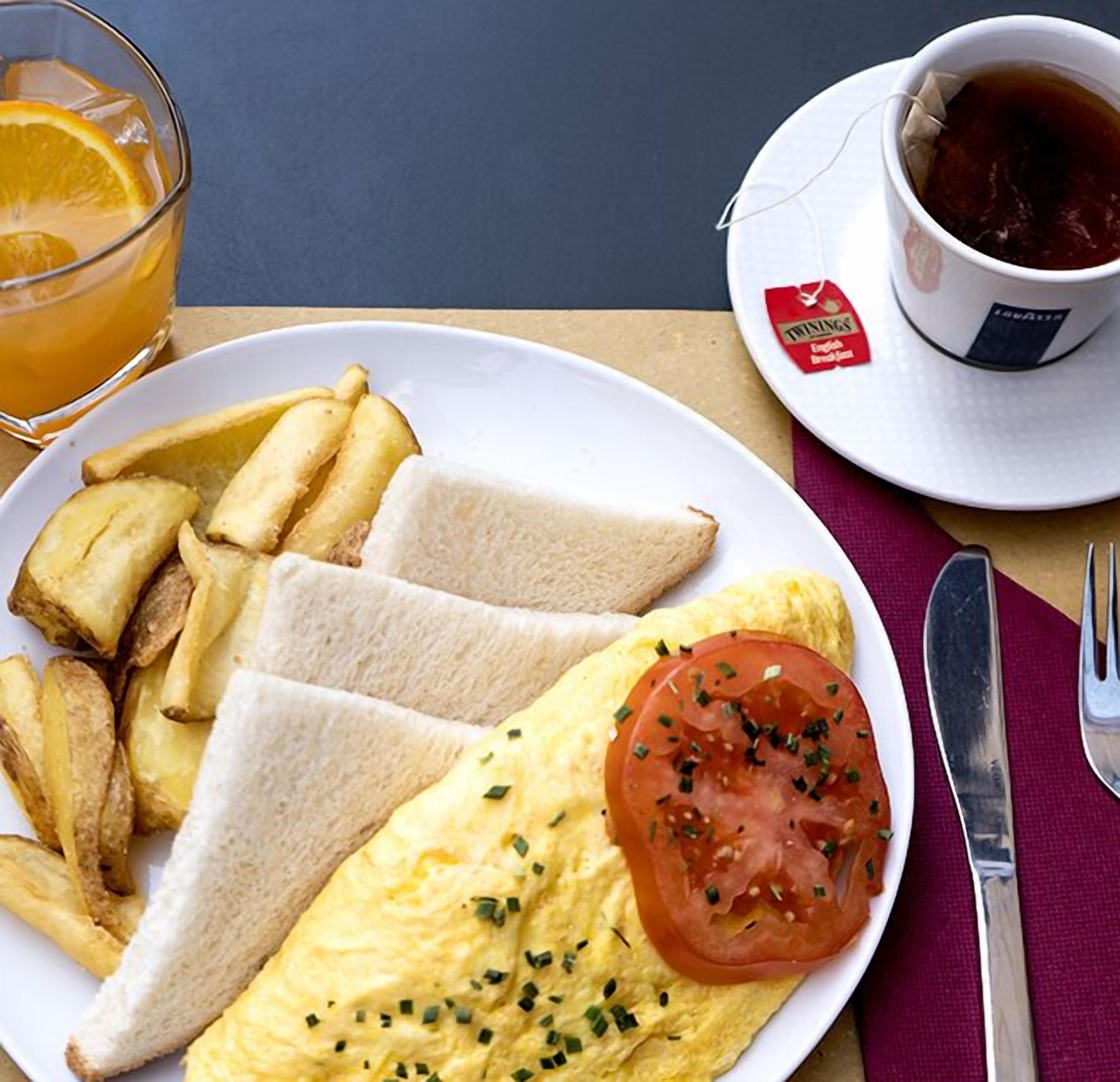 A breakfast plate with toast, fried potatoes, an omelette, and a tomato, accompanied by a cup of tea and a glass of orange juice.